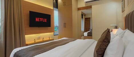 A hotel room with a bed, a TV mounted on the wall, an air conditioning unit, and a bedside table.