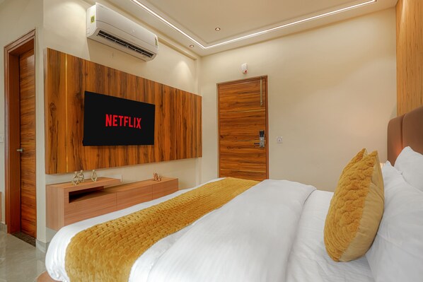 A modern bedroom with a large bed, a mounted TV displaying 'NETFLIX,' and a wooden wardrobe. - The Roseville Grand (Kharar)
