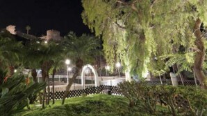 Ein Park bei Nacht mit einem Brunnen, Bäumen und einer Brücke.