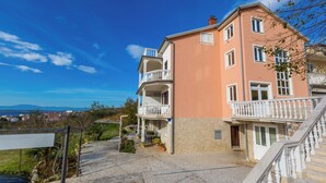 Un immeuble à plusieurs étages doté de balcons, d’une entrée pavée de pierres et offrant une vue sur le paysage.