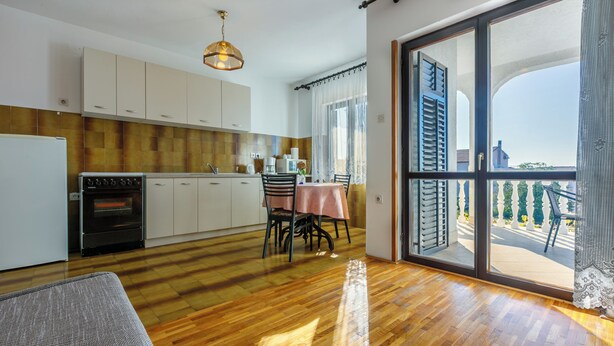 Une cuisine moderne avec un plancher en bois, un coin repas avec une table et des chaises, et une grande porte-fenêtre coulissante donnant sur un balcon extérieur.
