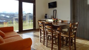 Un espace repas comprenant une table, des chaises, un téléviseur et une vue sur l’extérieur grâce à une grande fenêtre.