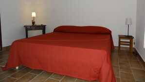 Un lit avec une couvre-lit rouge, une table de chevet avec une lampe et une petite table avec une autre lampe.