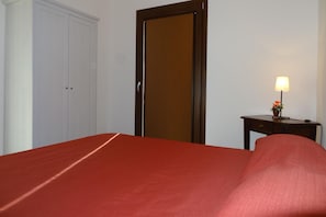 A room with a bed, a wooden door, a small table with a lamp, and a potted plant. - Apartment in Montefortino With Communal Pool (Montefortino)
