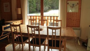 A wooden dining table with chairs, a window with curtains, and a view of trees. - Apartment Myrtilles for 6 People (Chatel)