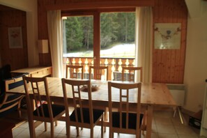 Ein Holztisch mit Stühlen, ein Fenster mit Vorhängen und Blick auf Bäume.