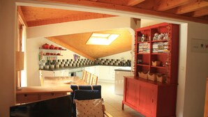 A kitchen with a wooden ceiling, a dining area with chairs and a table, and a red cabinet with shelves. - Apartment Myrtilles for 6 People (Chatel)