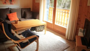 Ein gemütliches Wohnzimmer mit einer Couch, einem Holztisch, einem Sessel und einem Balkon mit Geländer.
