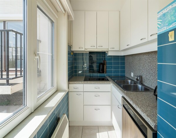 A modern kitchen with white cabinets, blue tiles, and a granite countertop. - Apartment in Blankenberge With Sea Views (Blankenberge)