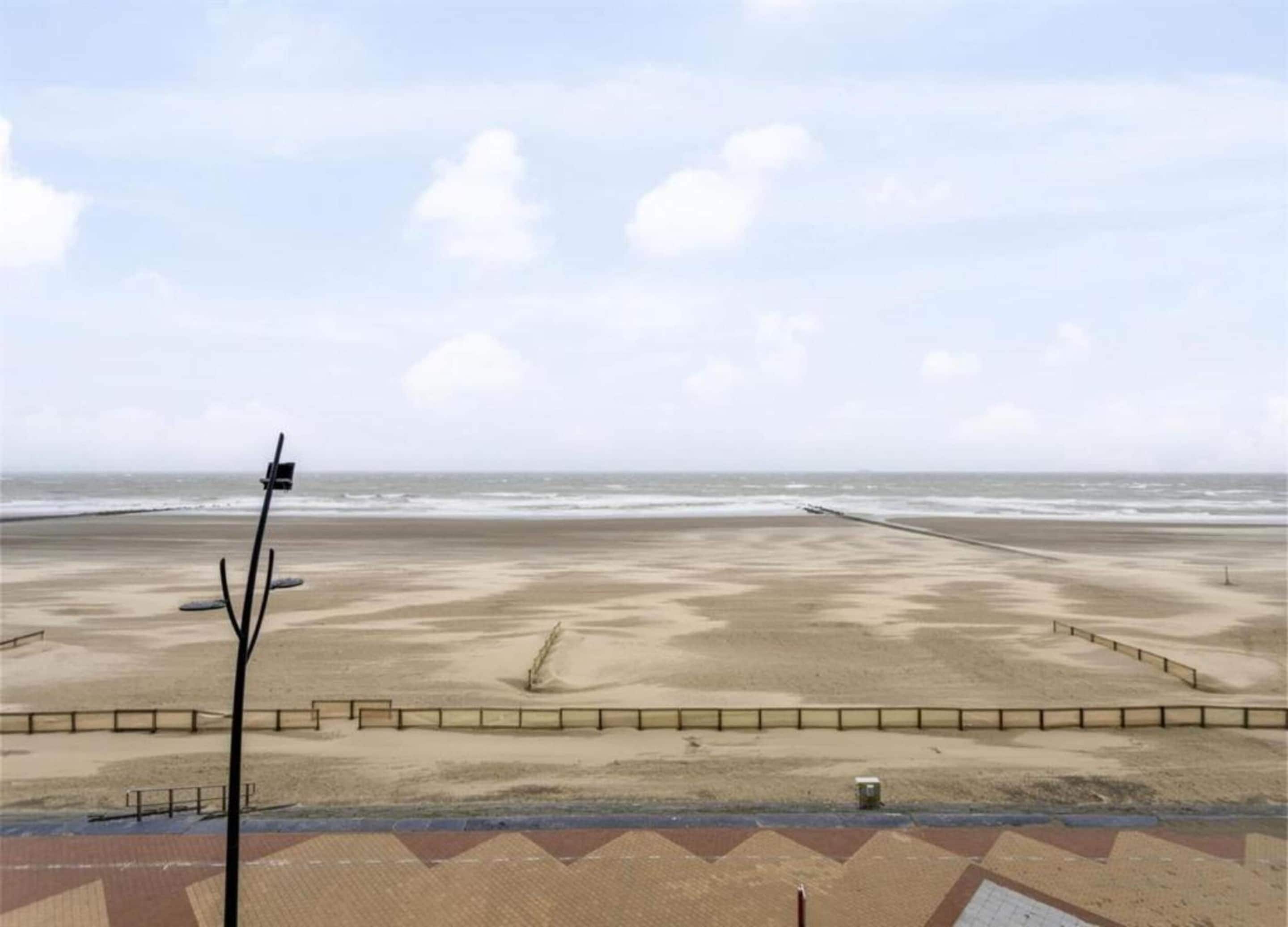 A beach view with a paved walkway, a metal fence, and a lamppost.