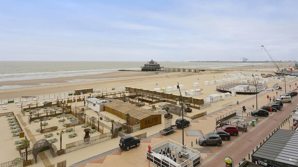 Ein Hotel am Strand mit einem Steg, Strandliegen und einem Parkplatz.