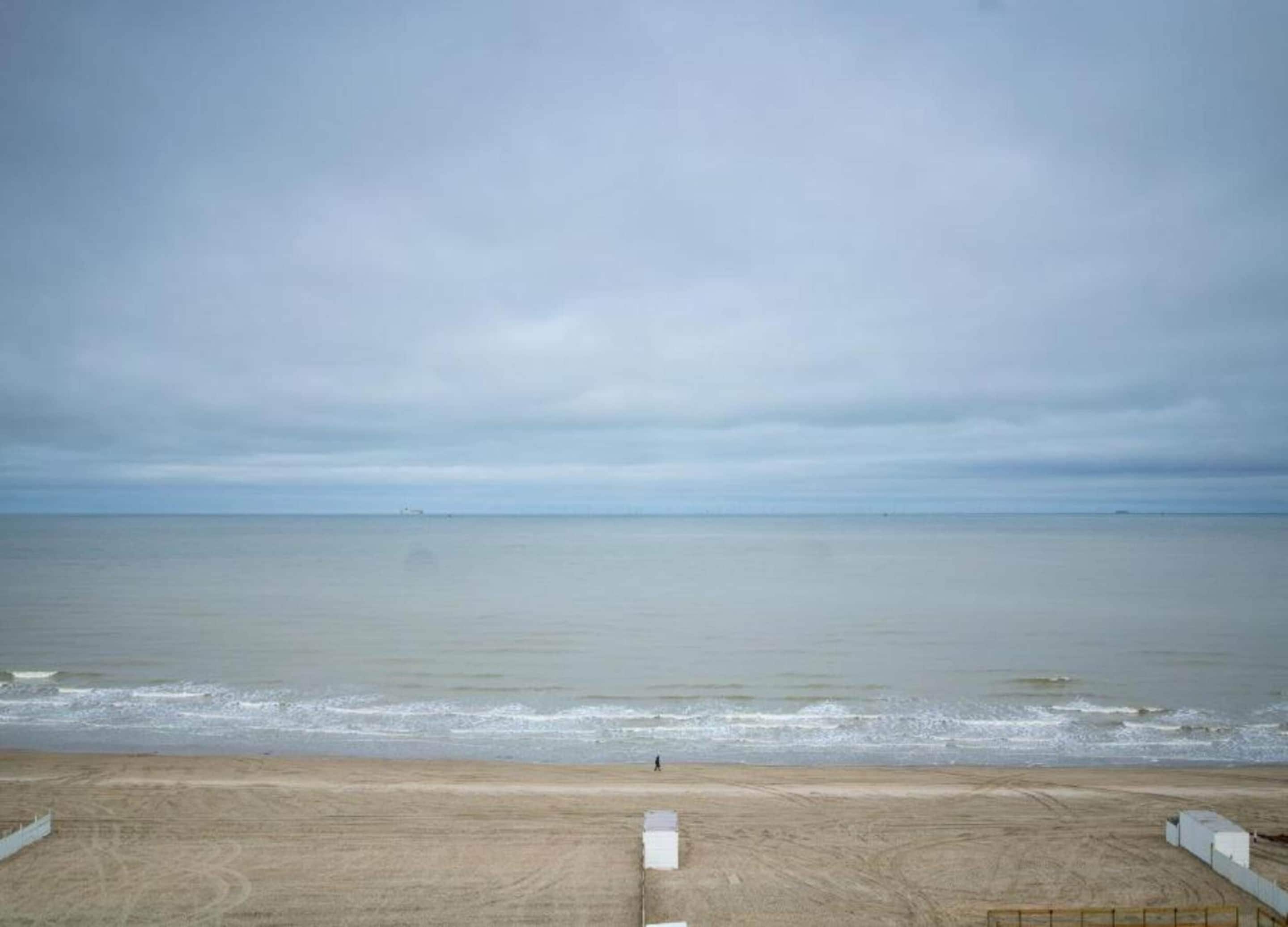 Blick auf einen Strand mit sandigem Vordergrund und ruhigem Meer unter einem bewölkten Himmel.