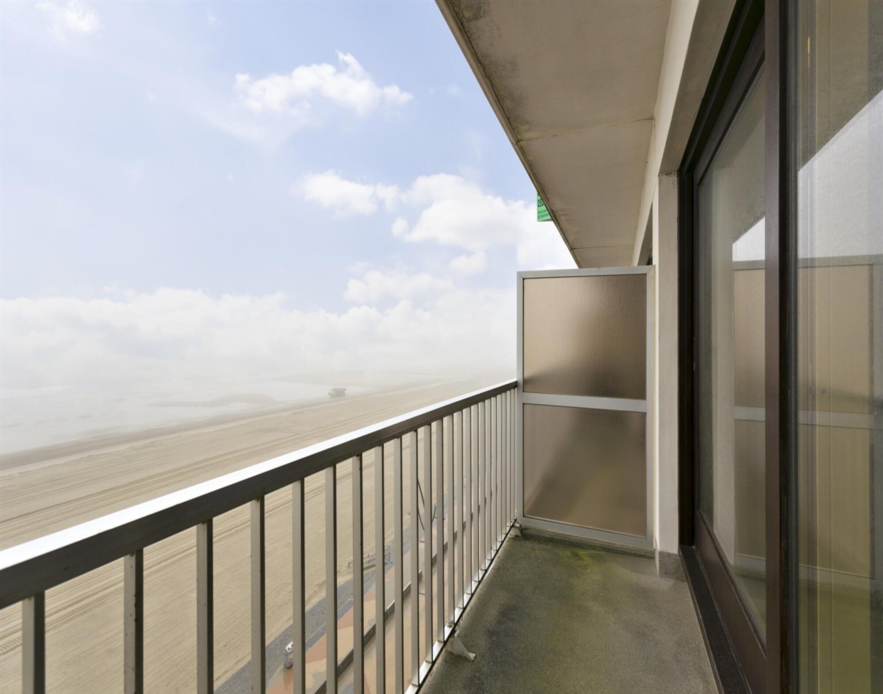 A balcony with a metal railing, a glass door, and a view of a beach and sky.