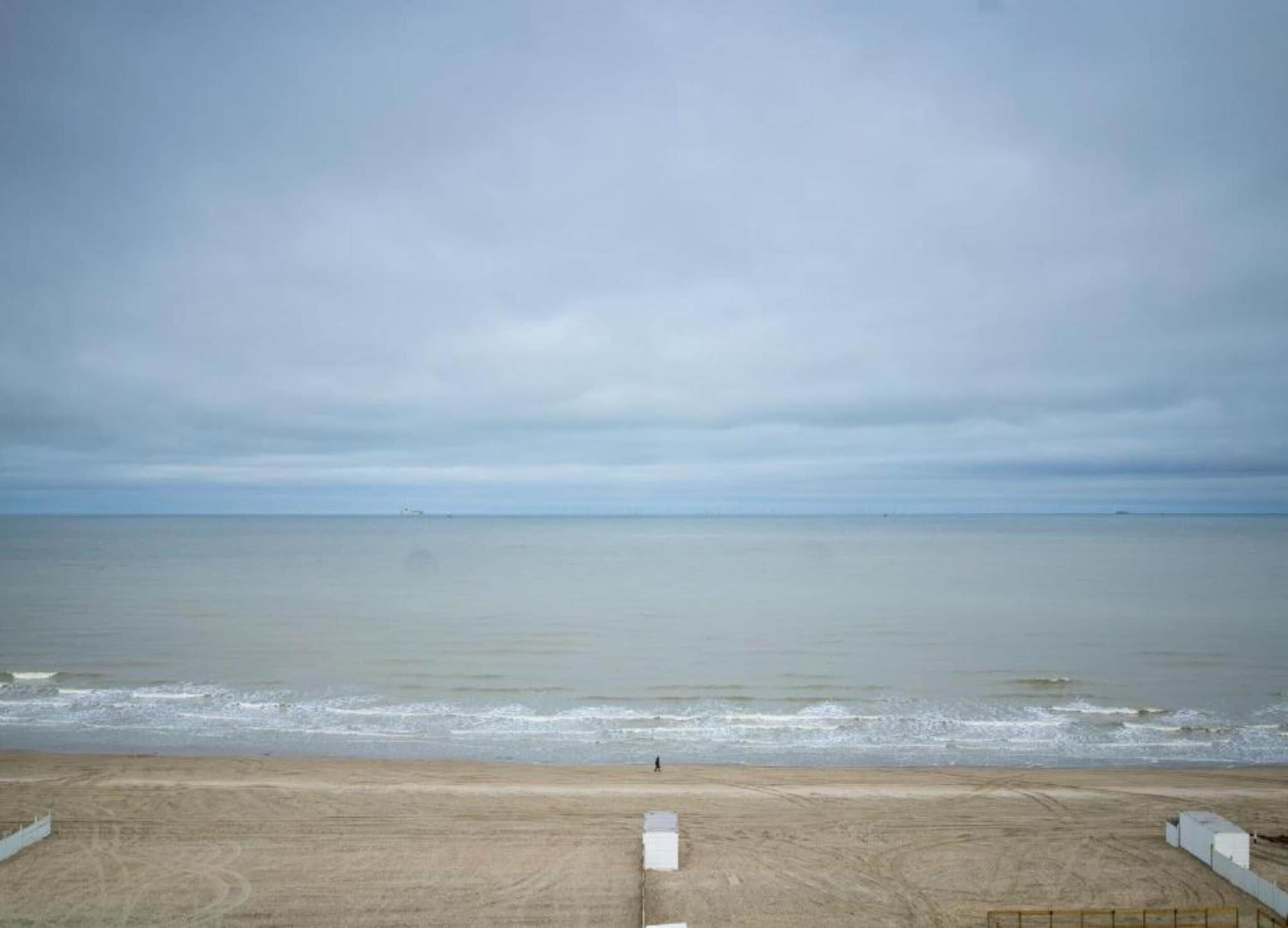 A beach view with a sandy foreground and a calm sea under a cloudy sky.
