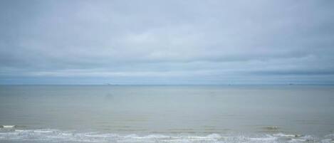 A beach view with a sandy foreground and a calm sea under a cloudy sky.