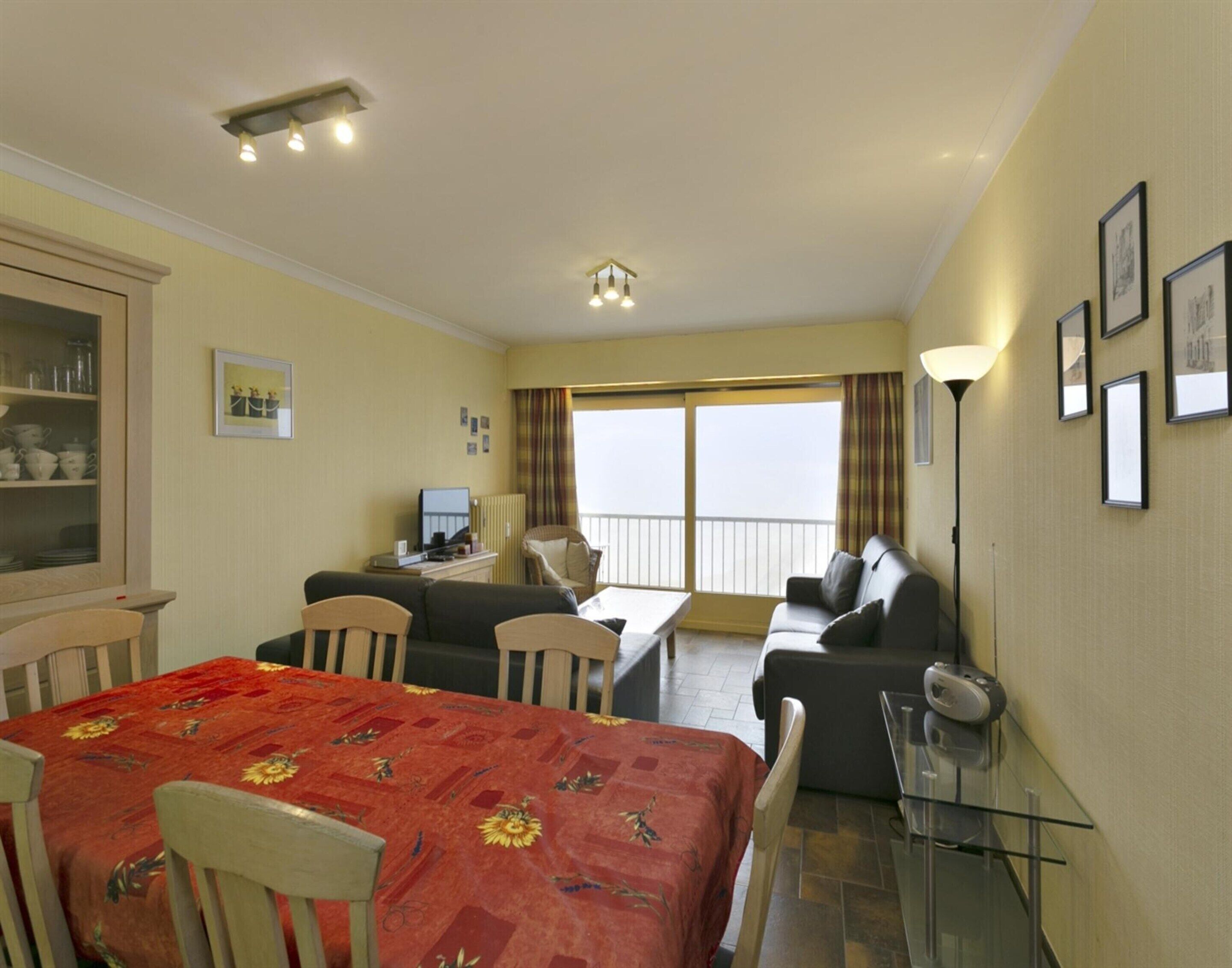 A hotel room with a dining area, a sofa, a TV, and a balcony with curtains.