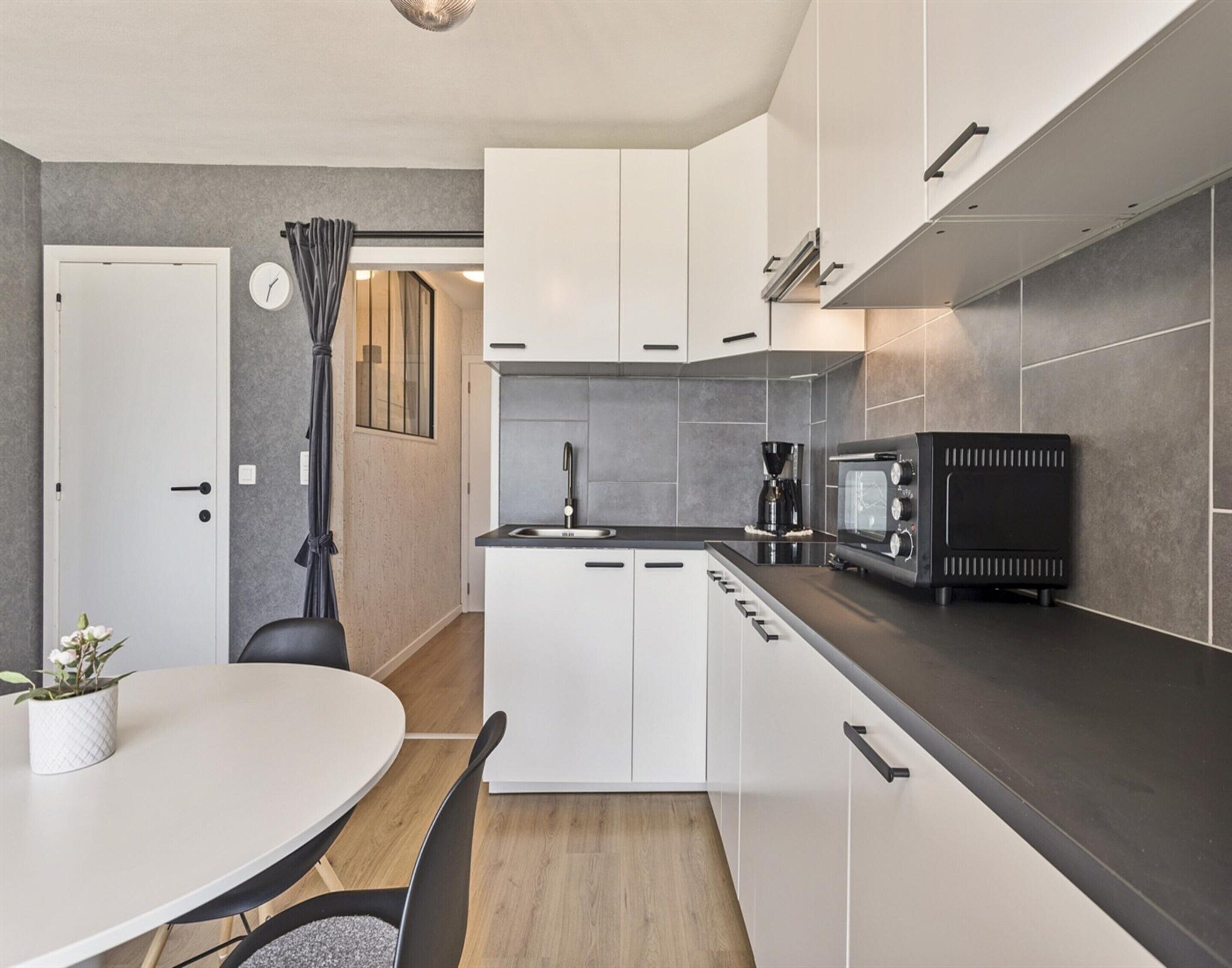 A modern kitchen with white cabinets, a black countertop, a microwave, and a coffee maker.