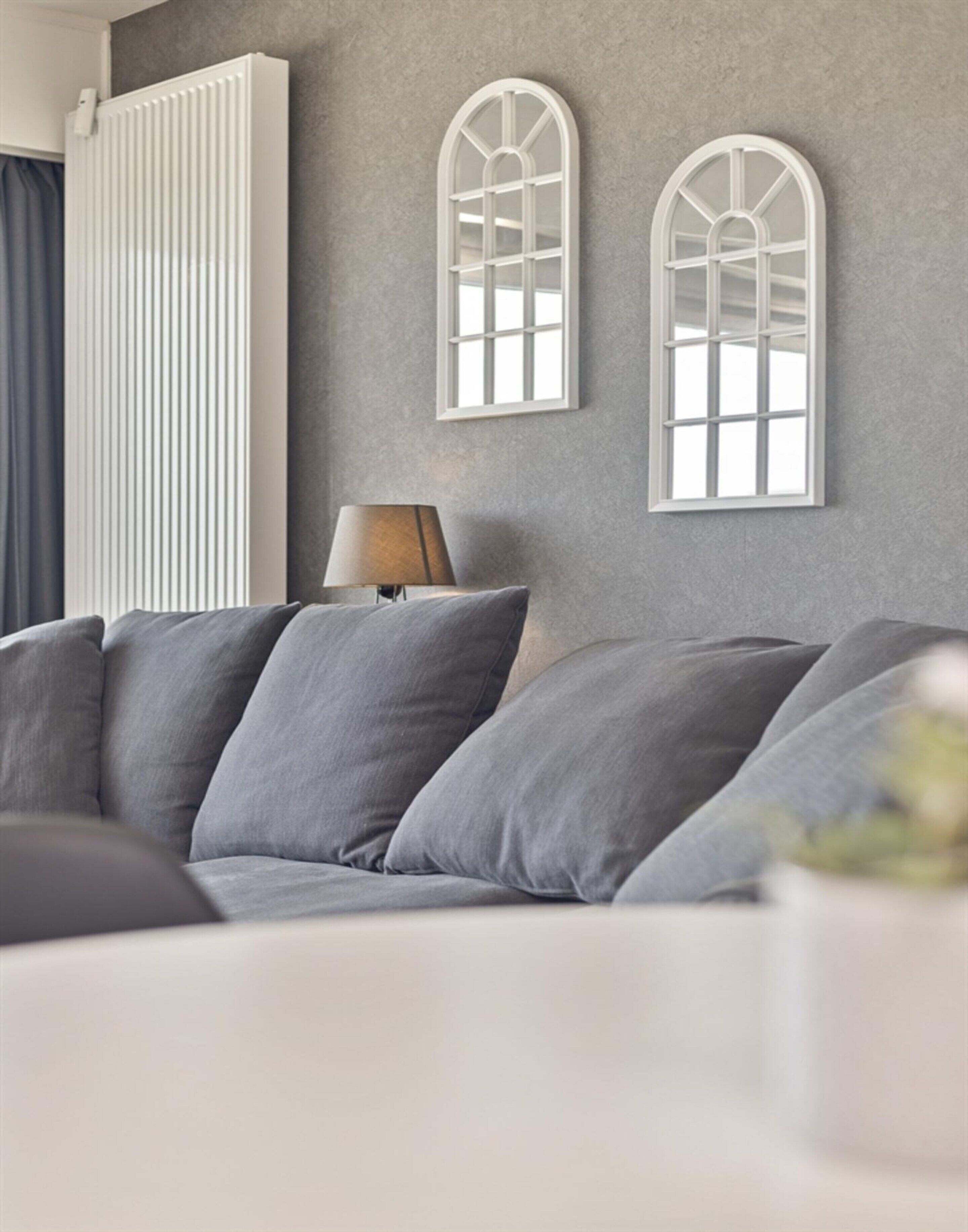 Un salon moderne avec un canapé gris, un radiateur blanc et deux appliques murales en forme d’arc.