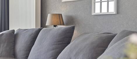 Un salon moderne avec un canapé gris, un radiateur blanc et deux appliques murales en forme d’arc.