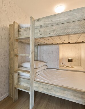 Ein Etagenbett mit Holzrahmen, ein Nachttisch mit Lampe und eine Wand mit strukturierter Oberfläche.
