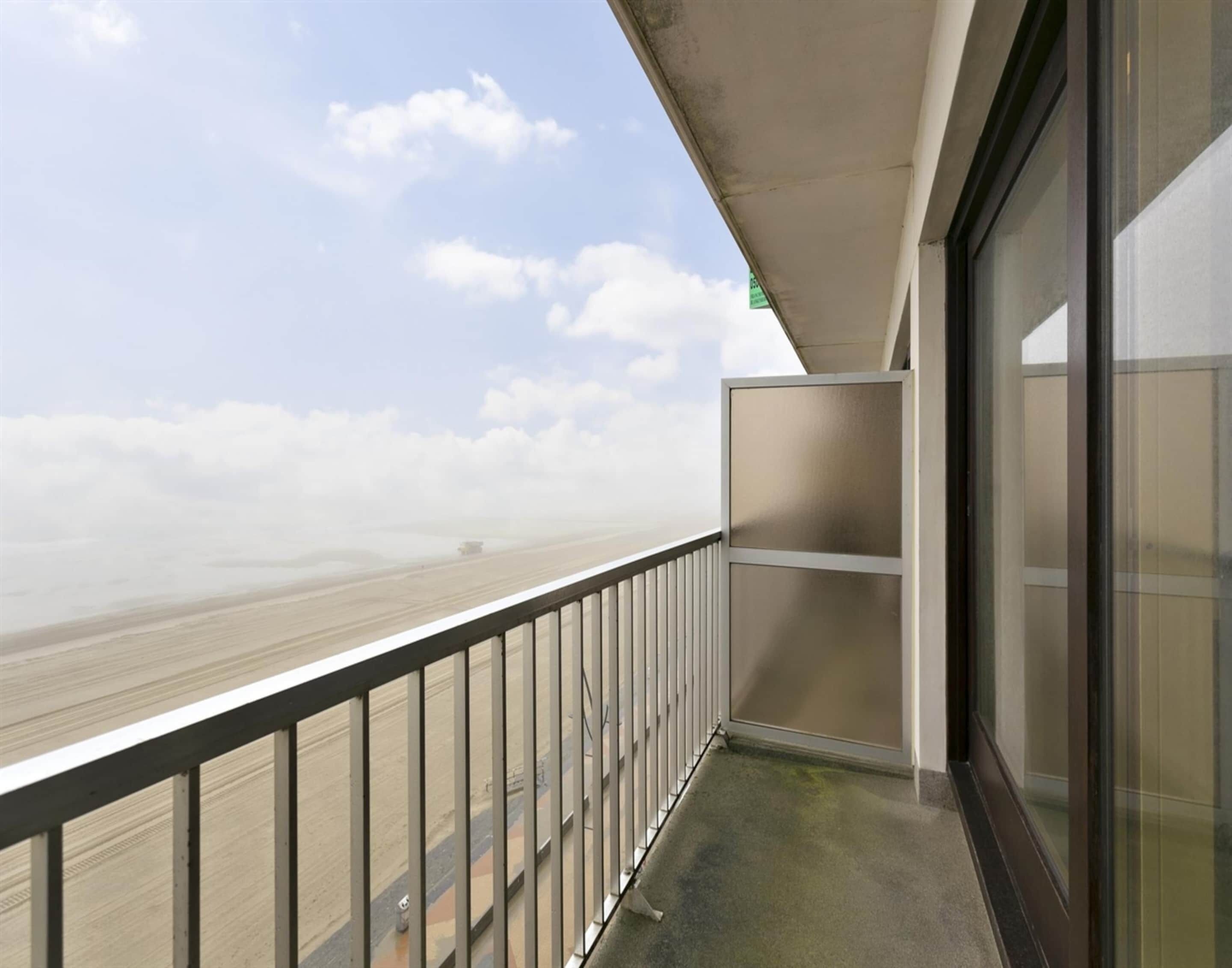 A balcony with a metal railing, a glass door, and a view of a beach.
