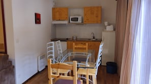 A compact kitchen with wooden cabinets, a microwave, a sink, and a dining table with chairs. - Apartment Near Centre of Orelle (Orelle)
