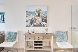 A room with a white desk, two white chairs, a painting of a woman by the sea, and a radiator. - Apartment in Blankenberge With Sea Views (Blankenberge)