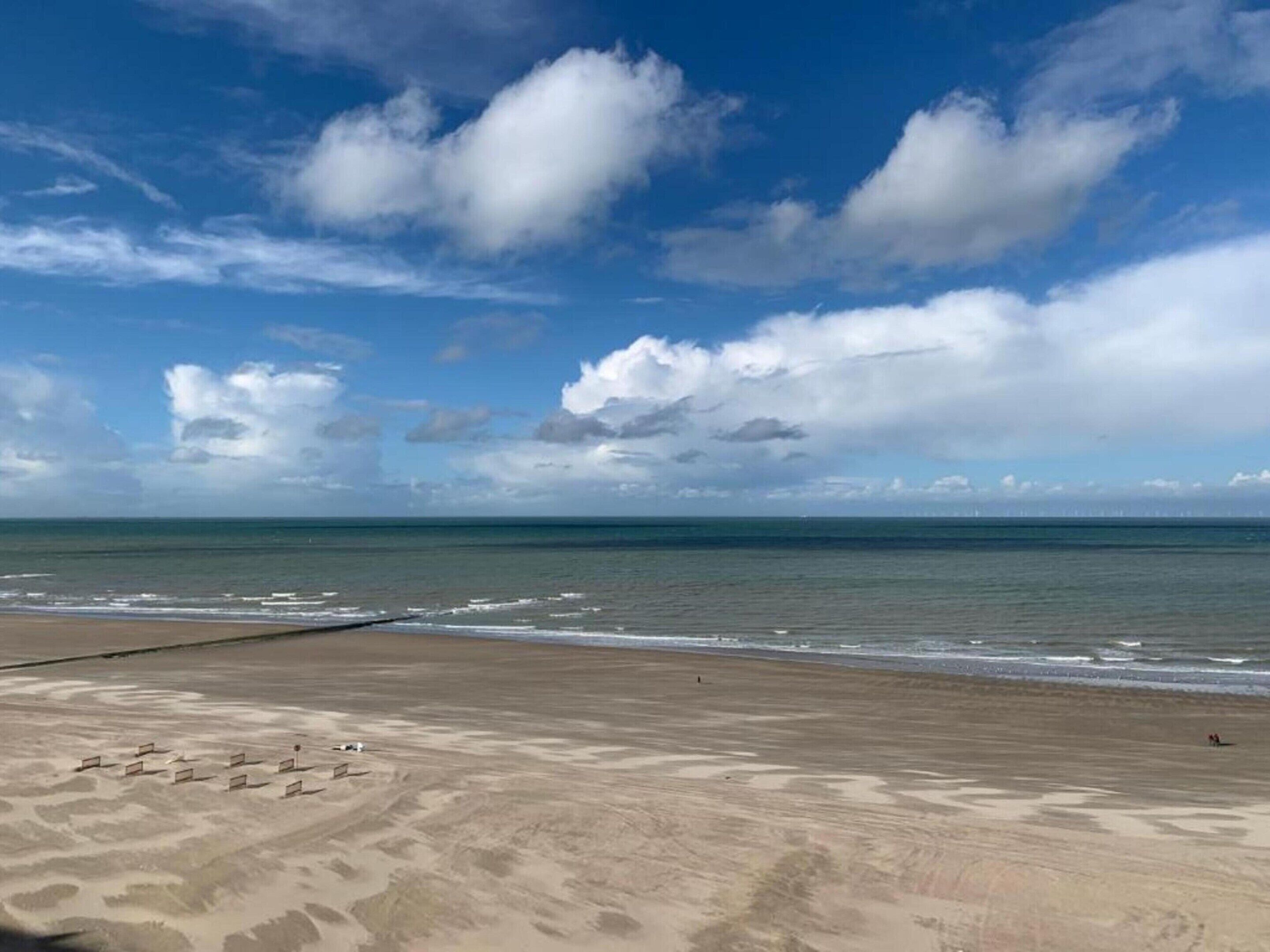 A beach with a clear sky, calm sea, and a few people in the distance.