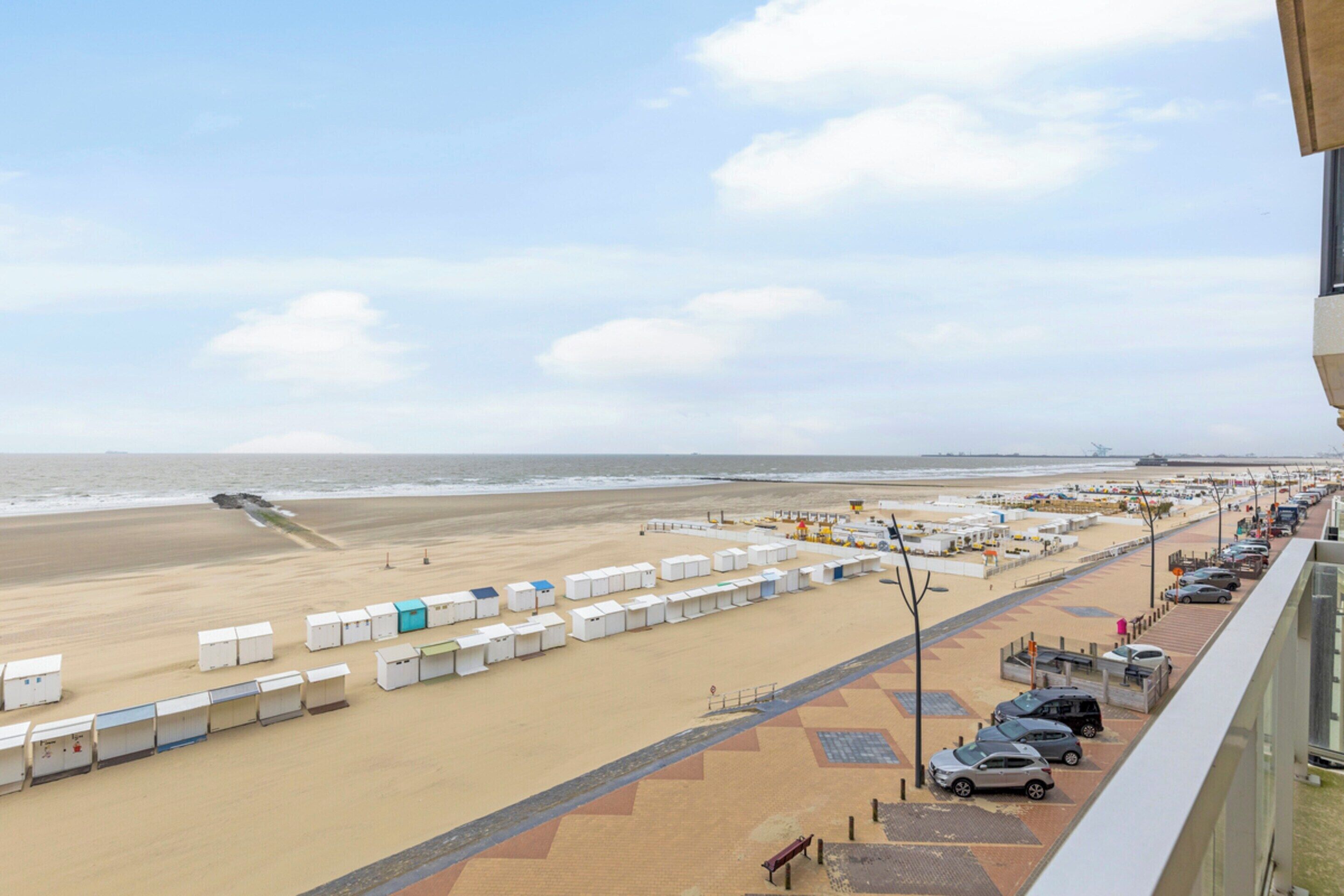 Um hotel à beira-mar com fileiras de cabanas de praia, um estacionamento e vista para o oceano.