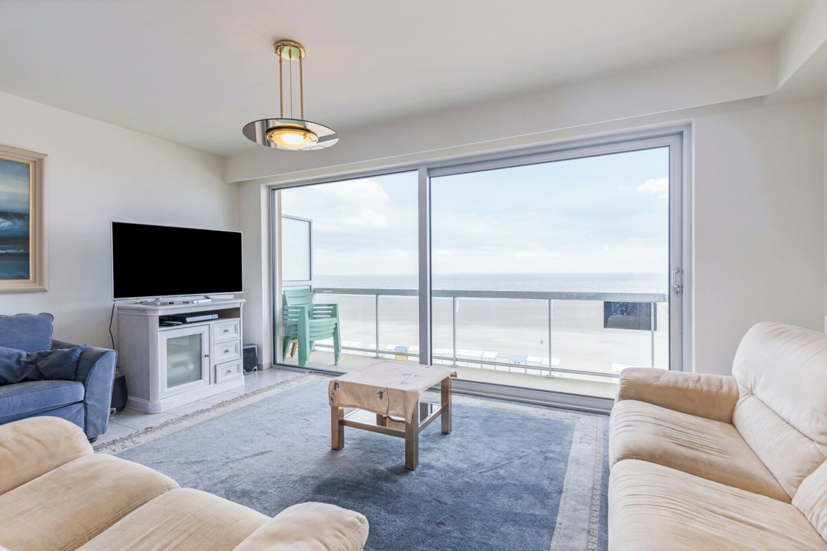 A living room with a large window, a flat-screen TV, a sofa, a coffee table, and a small table.