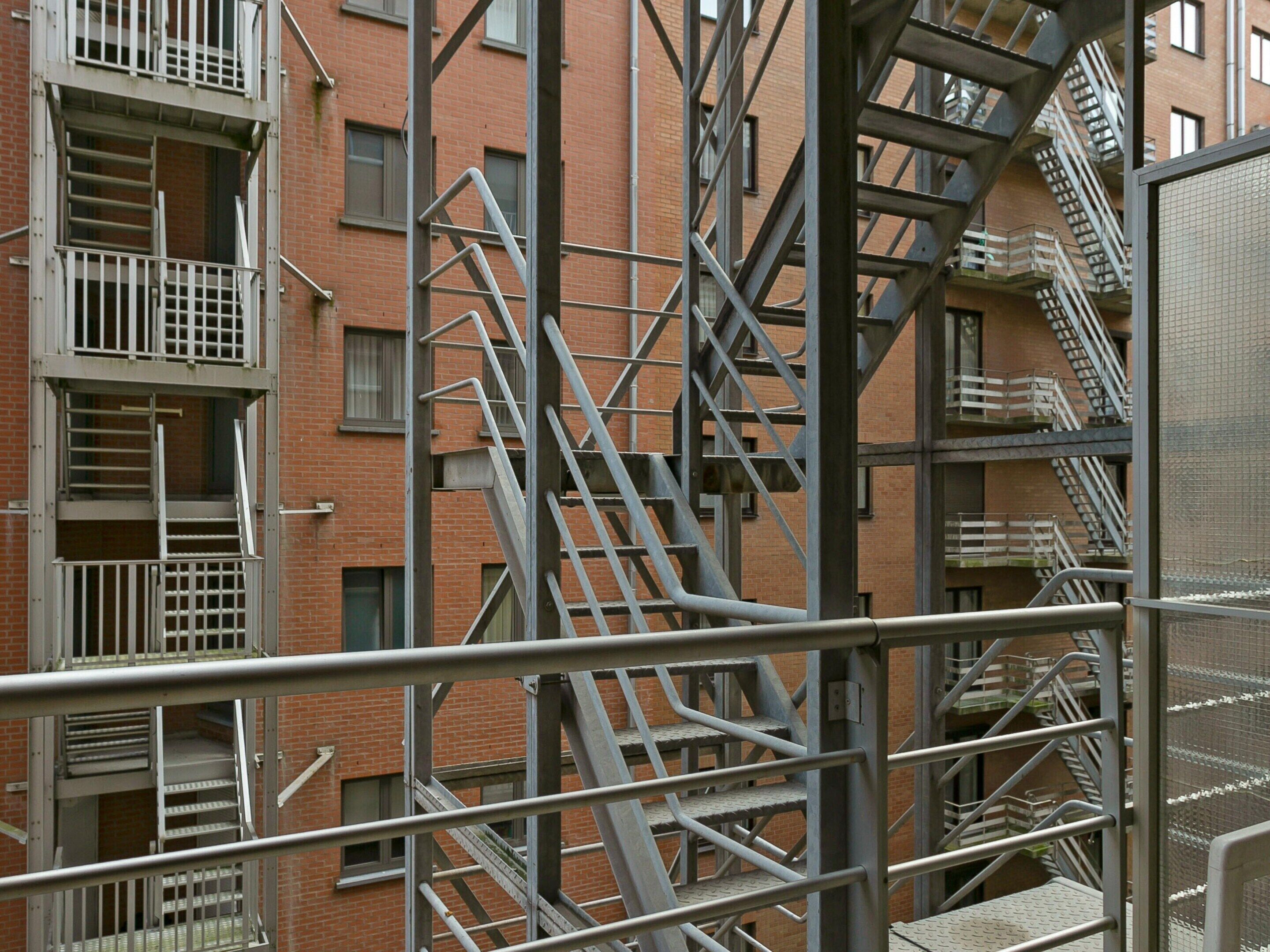 Un edificio de varios pisos con escaleras de emergencia externas y una barandilla de metal en primer plano.