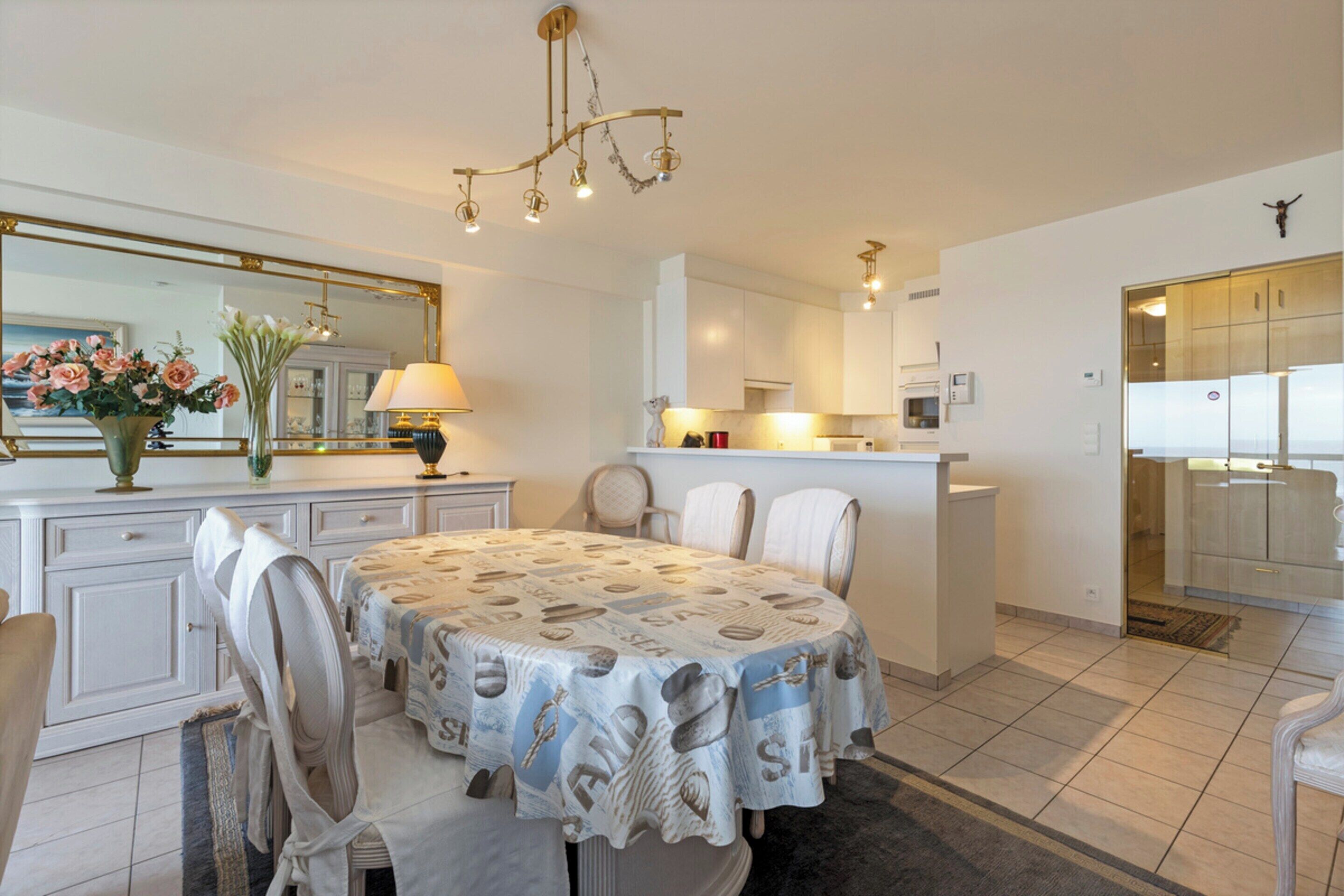 Una cocina moderna con armarios blancos, una isla central y una zona de comedor con mesa y sillas.