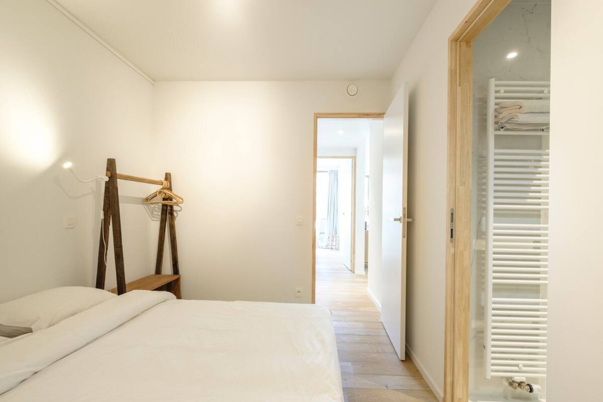 Ein Schlafzimmer mit einem Bett, einem hölzernen Kleiderbügel und einem Flur, der zu einem Badezimmer mit einem weißen Heizkörper führt.