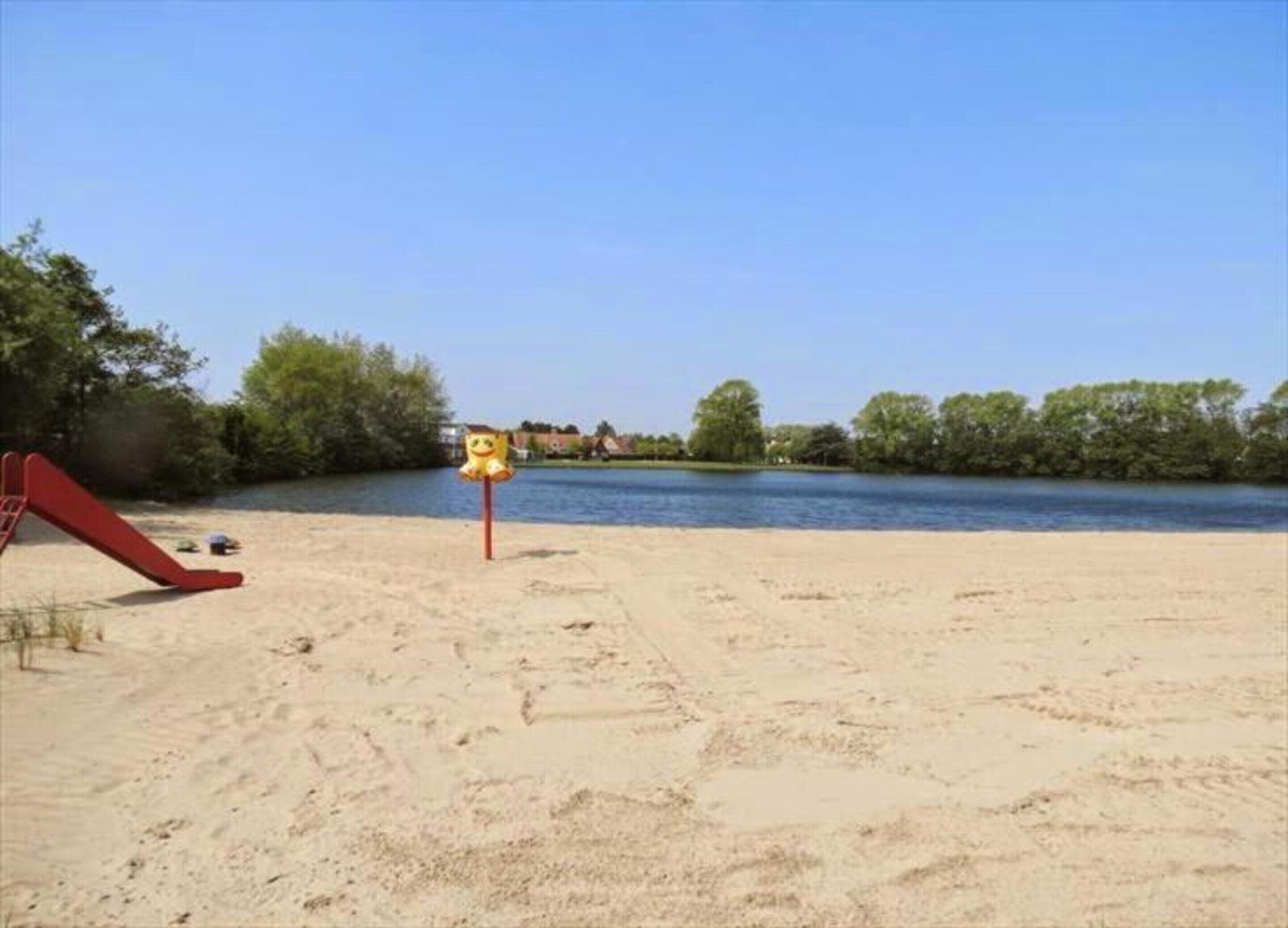 Una spiaggia sabbiosa con uno scivolo rosso e un segnale giallo.