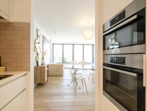 A modern kitchen with stainless steel appliances, a dining area with a glass table and chairs, and a brick accent wall. - Apartment Knokke-heist With Sea View (Knokke-Heist)