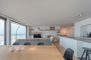 Un espacio de estar moderno con comedor, cocina y un ventanal con vistas a la playa.