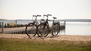 Three bicycles parked on a sandy area near a body of water with a wooden pier in the background. - Seepark Heidenholz, Plau am See (Plau am See)