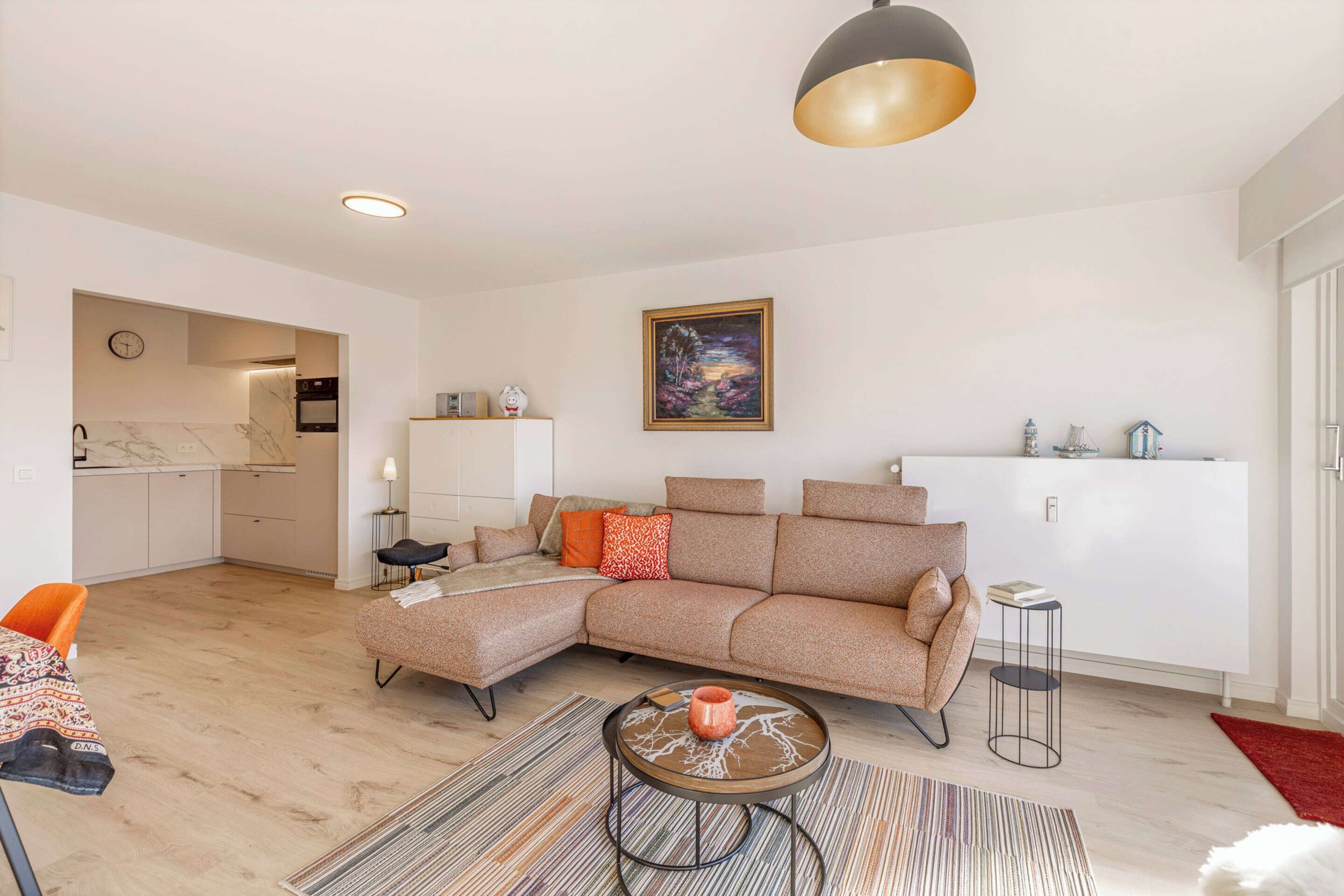 A modern living room with a sectional sofa, a coffee table, a dining area with a chair, and a kitchen in the background.