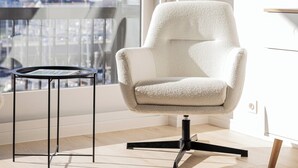 En moderne stol med høj ryg og metalstel, placeret ved et vindue med udsigt over bybilledet.