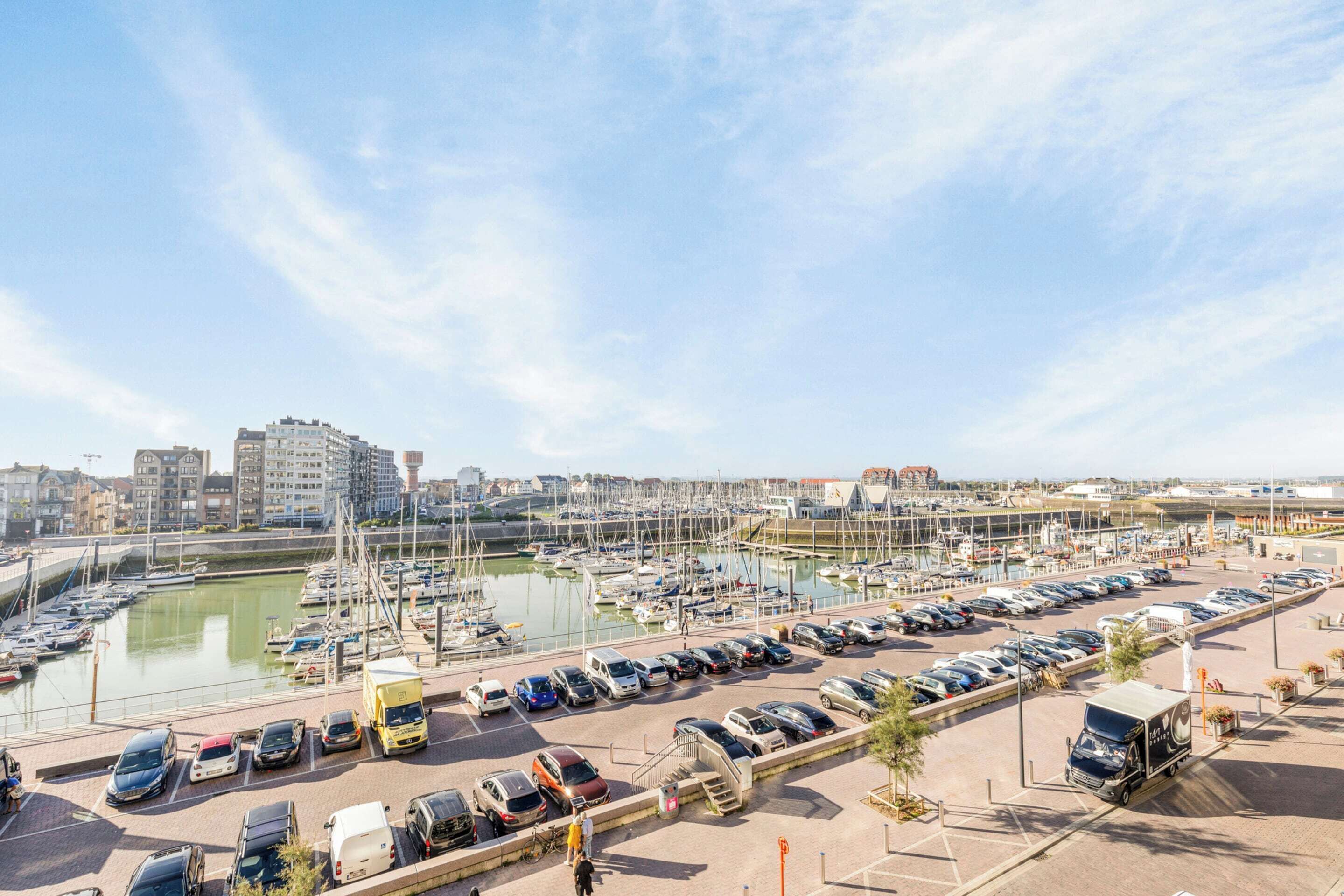 A marina with boats, a parking lot, and buildings in the background.