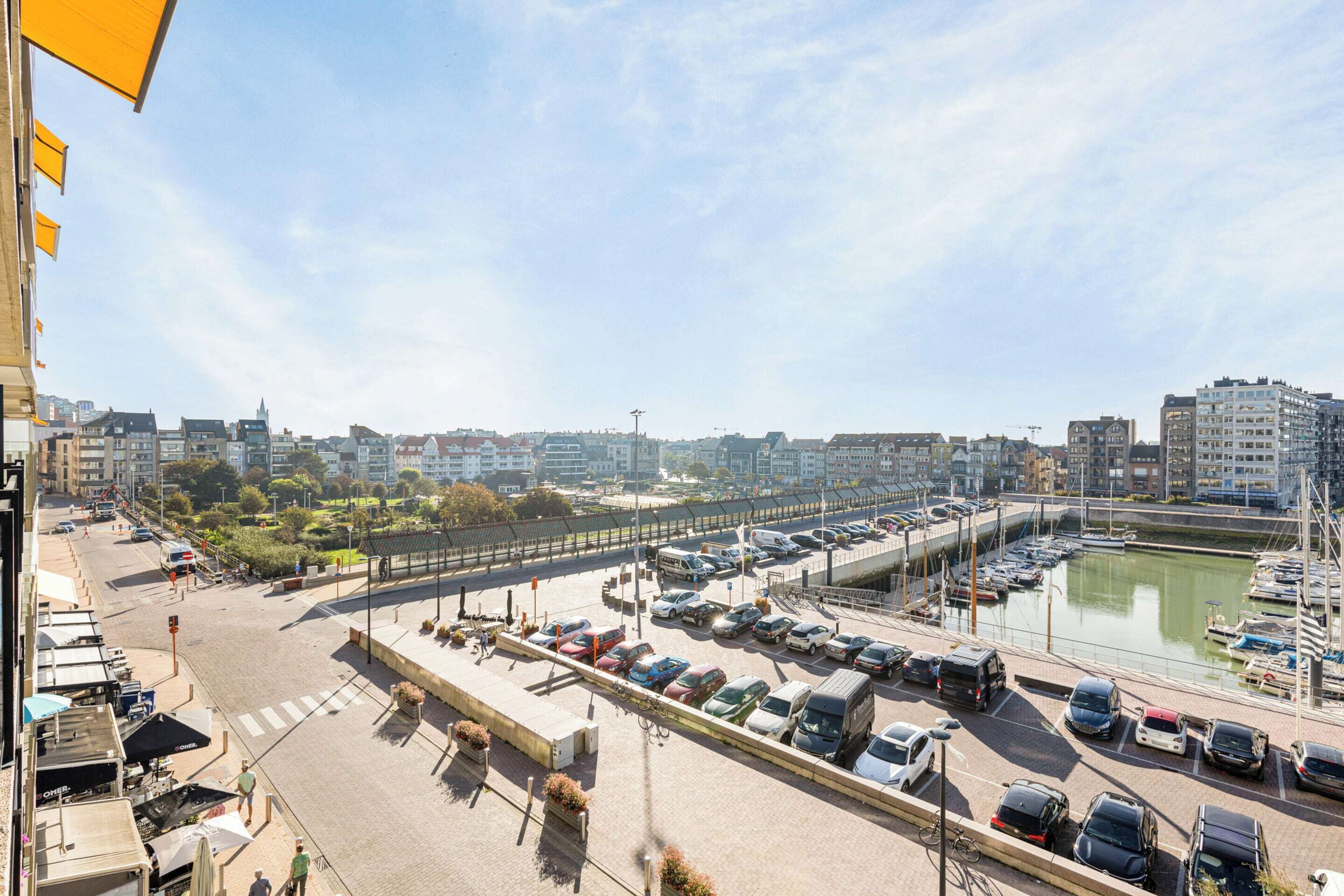 A marina with boats, a parking lot with cars, and buildings in the background.
