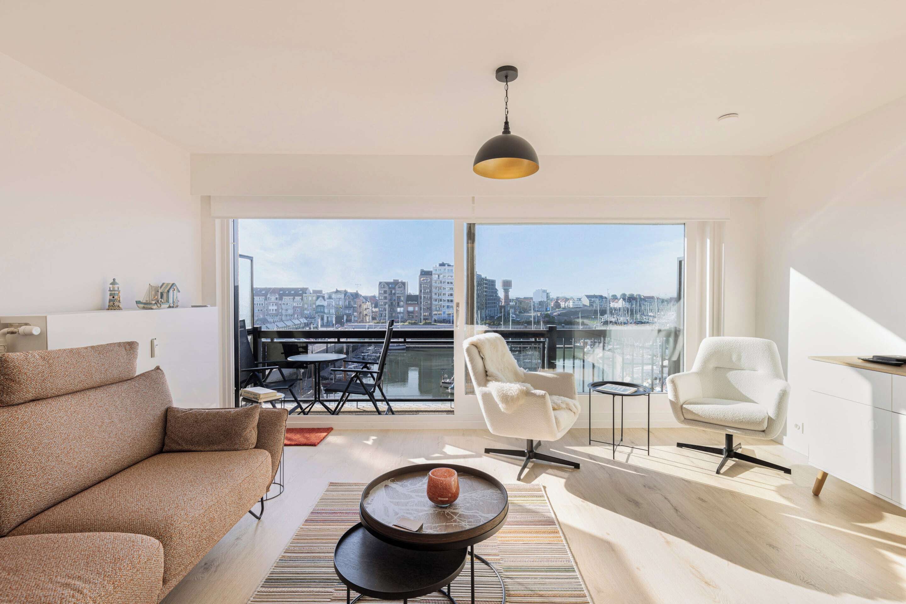 A modern living room with a sofa, two chairs, a small table, and a large window with a city view.