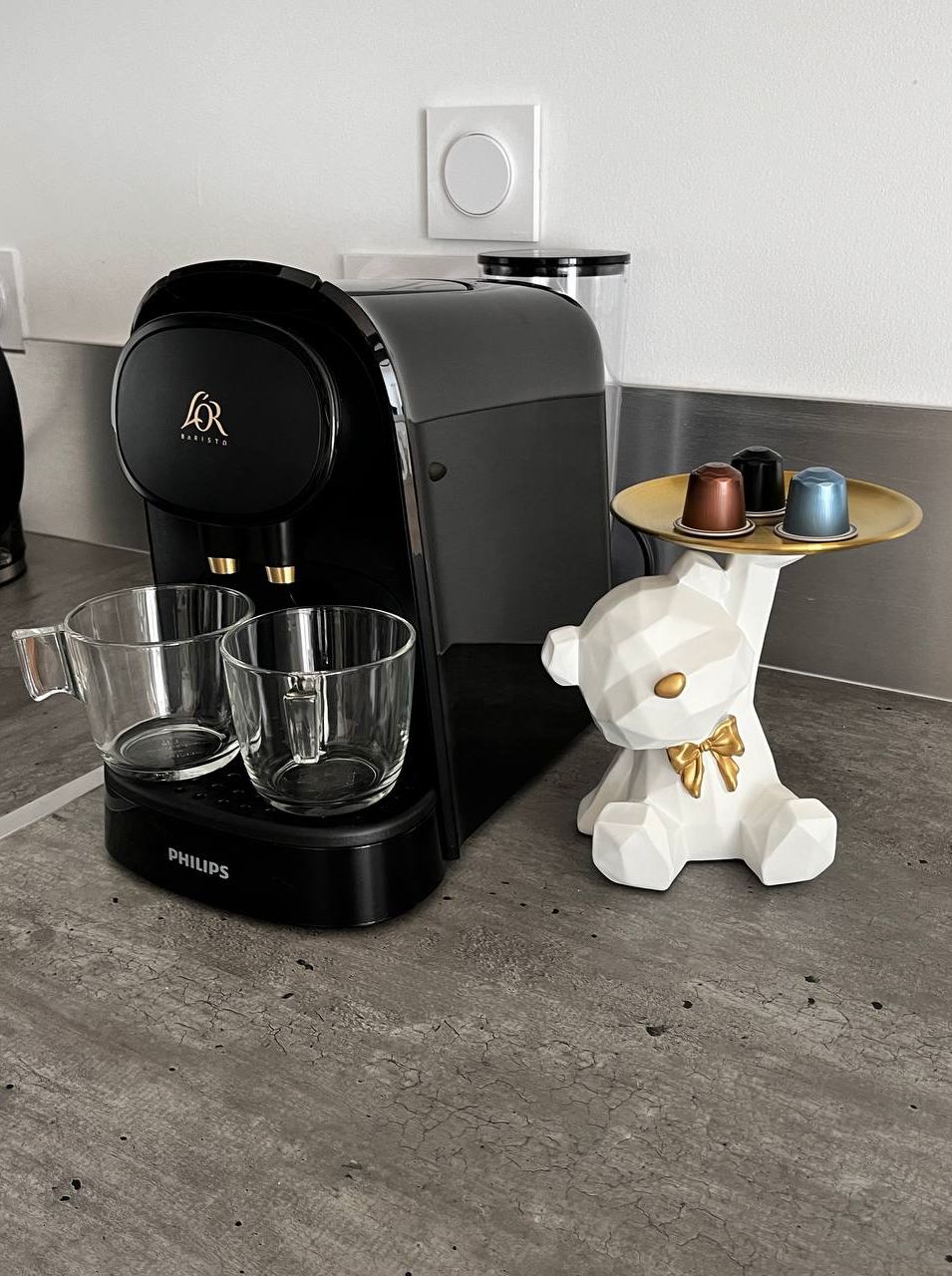 Een koffiezetapparaat, twee glazen en een decoratief berenbeeldje op een aanrecht.