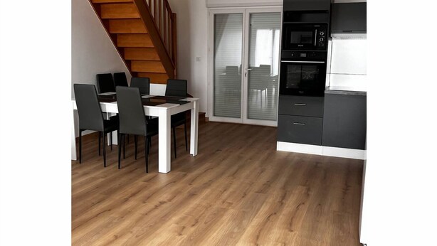 Une cuisine moderne équipée d’un four à micro-ondes, d’un four et de placards, un coin repas avec une table et des chaises, et un escalier en bois.