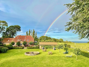 A house with a red roof, a circular stone fountain, and a grassy yard with a view of the sea. - Hof Kracht – "Jaromar" One-Bedroom Apartment for 2 People on the Baltic Sea (Putgarten)