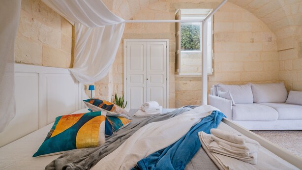 A room with a bed, a white sofa, a window with curtains, and a stone wall.