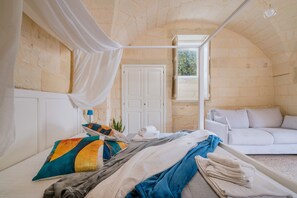 A room with a bed, a white sofa, a window with curtains, and a stone wall.