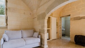A stone-walled room with a white sofa, a wooden barrel, and a doorway leading to another room.