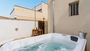 A hot tub in a courtyard with a table and chairs, a lamp post, and a building with a window.