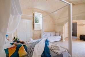 Un dormitorio con cama con dosel, un sofá blanco y vistas a un espacio exterior.